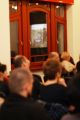 Publiczność na sali. W tle okno z odbiciem gościa